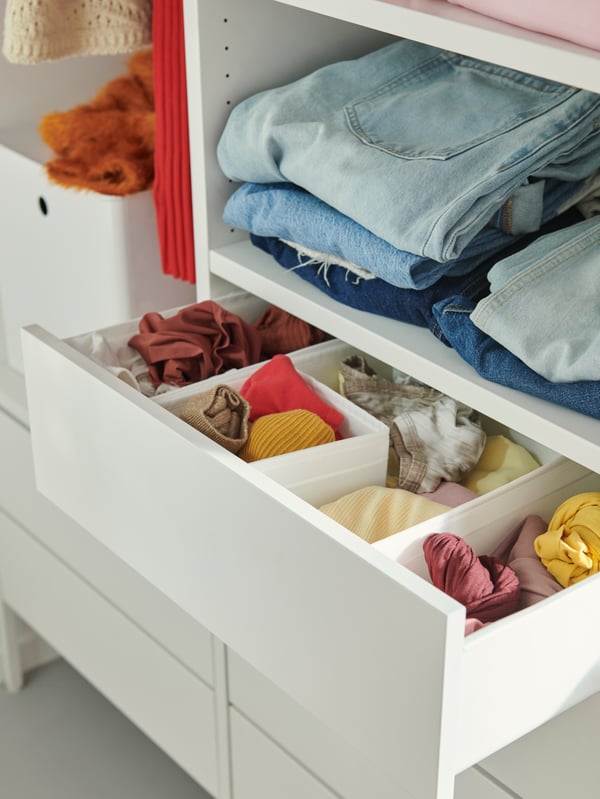 A close-up of the drawers and shelves of a white AURDAL wardrobe with clothes folded on the shelves and in the drawers.