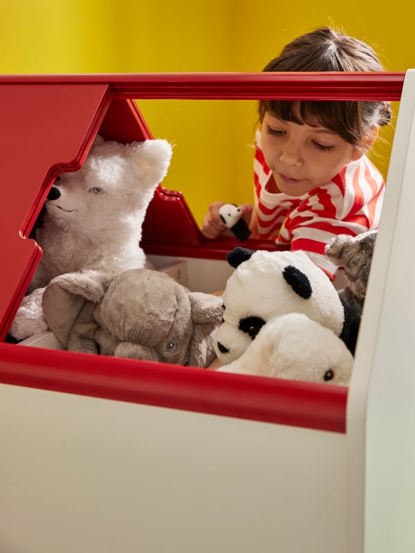 Una niña eligiendo entre una variedad de peluches IKEA que están dentro de un mueble VITBJÖRN.