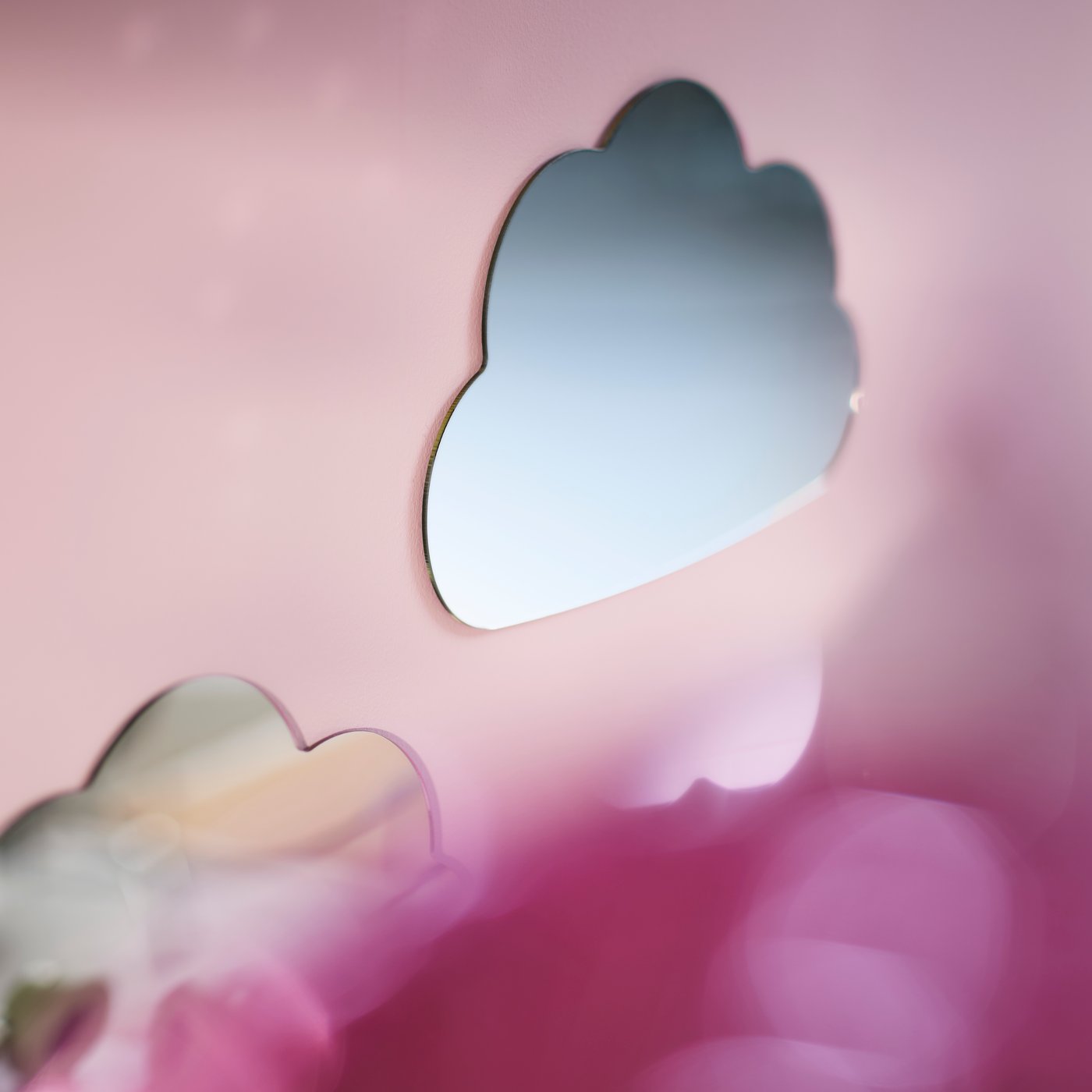 Sur un mur rose d’une chambre d’enfant, miroir HOLMÖARNA en forme de nuage au-dessus d’un lit avec une literie colorée.