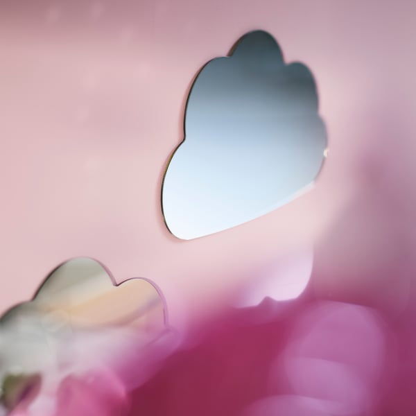 HOLMÖARNA mirror in a cloud shape mounted on a pink wall above a bed with colourful bedding in a children’s bedroom.
