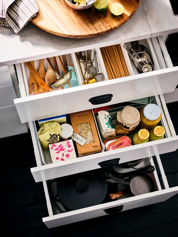 A column of drawn-out, white drawers, revealing neatly organized pantry-compatible bottles, jars and kitchen accessories.