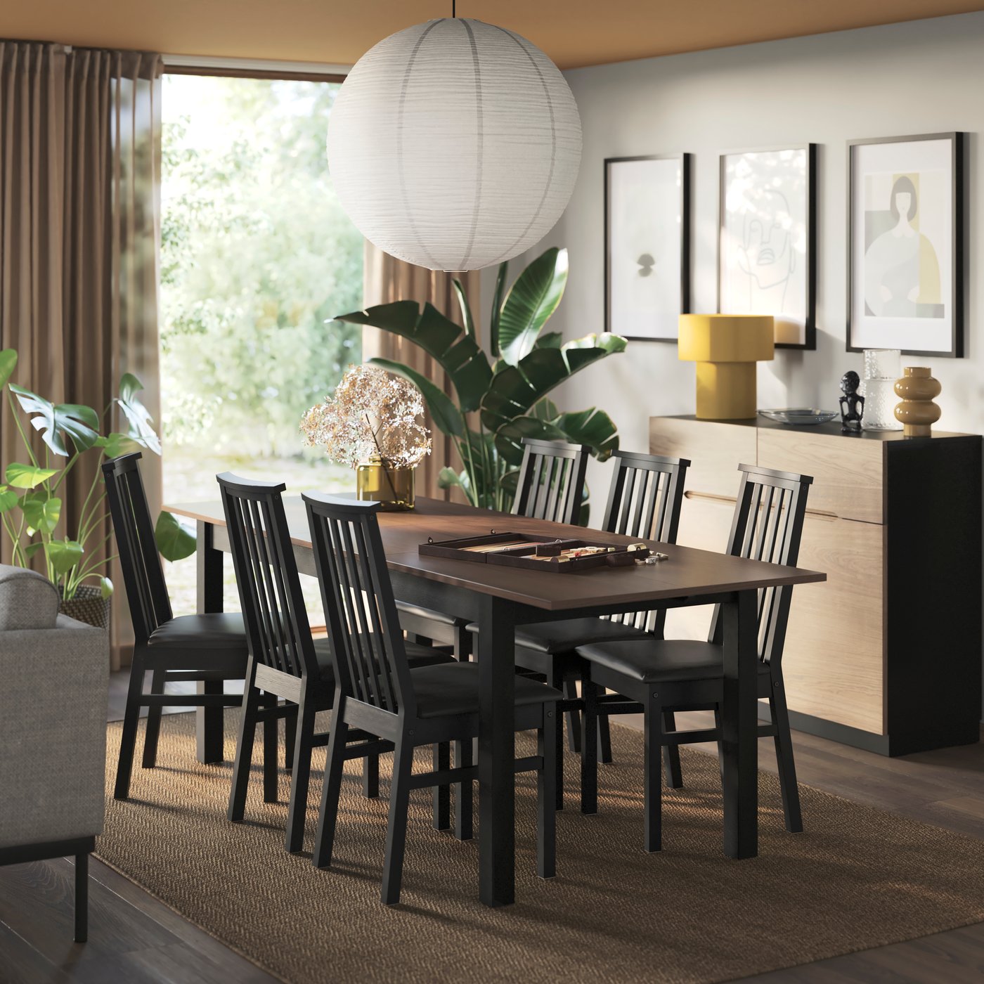 A black and brown IKEA ÅLHULT dining table and six chairs in a dining room, with a jute rug and a large paper-sphere ceiling pendant lamp above.