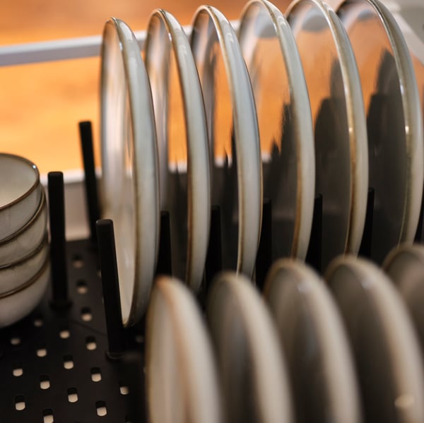 An anthracite UPPDATERA pegboard drawer organiser inside an open drawer, holding a collection of side plates and bowls.