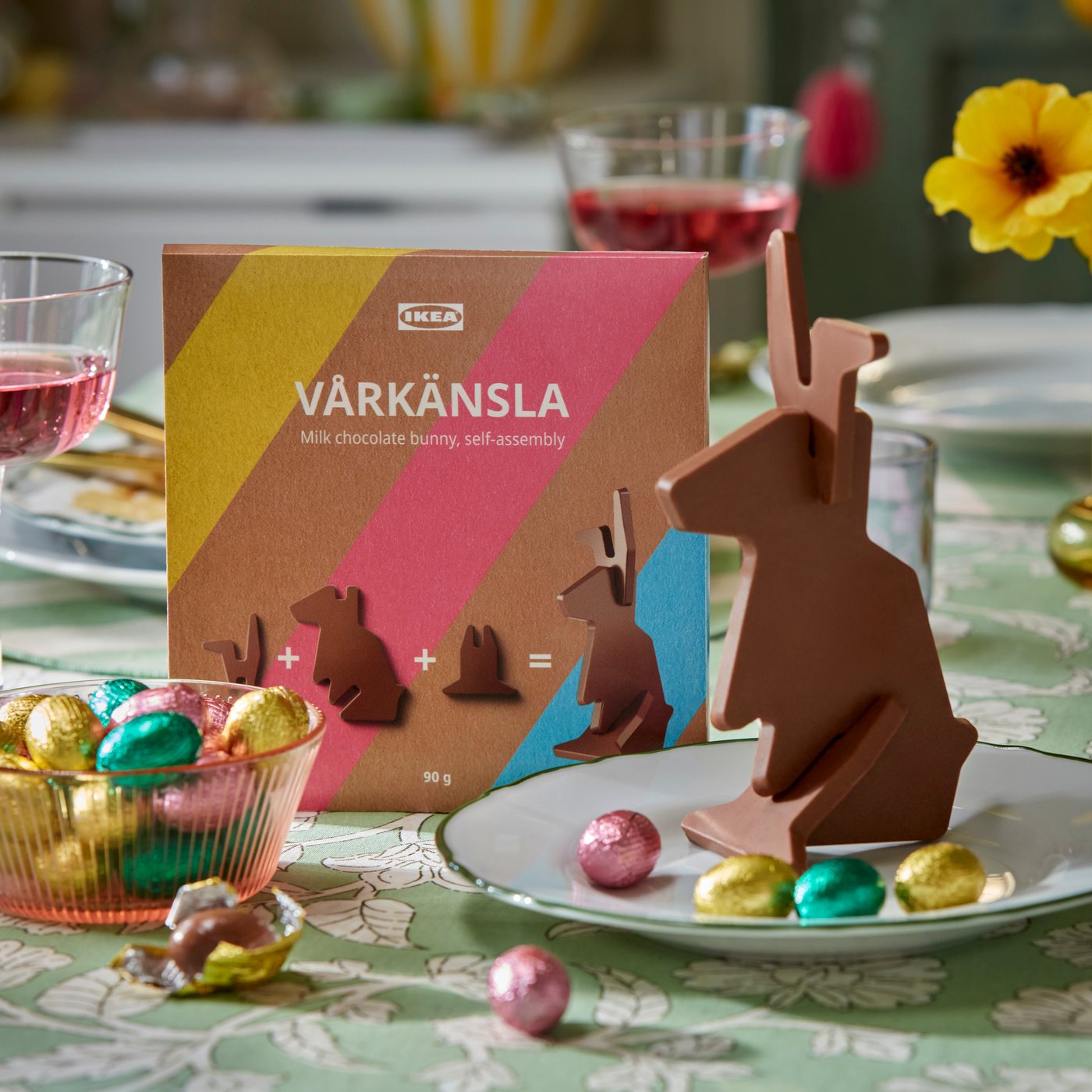 Een close-up van een VÅRKÄNSLA melkchocoladehaasje en enkele kleurrijke VÅRKÄNSLA melkchocolade-eieren in een decoratieve schaal.