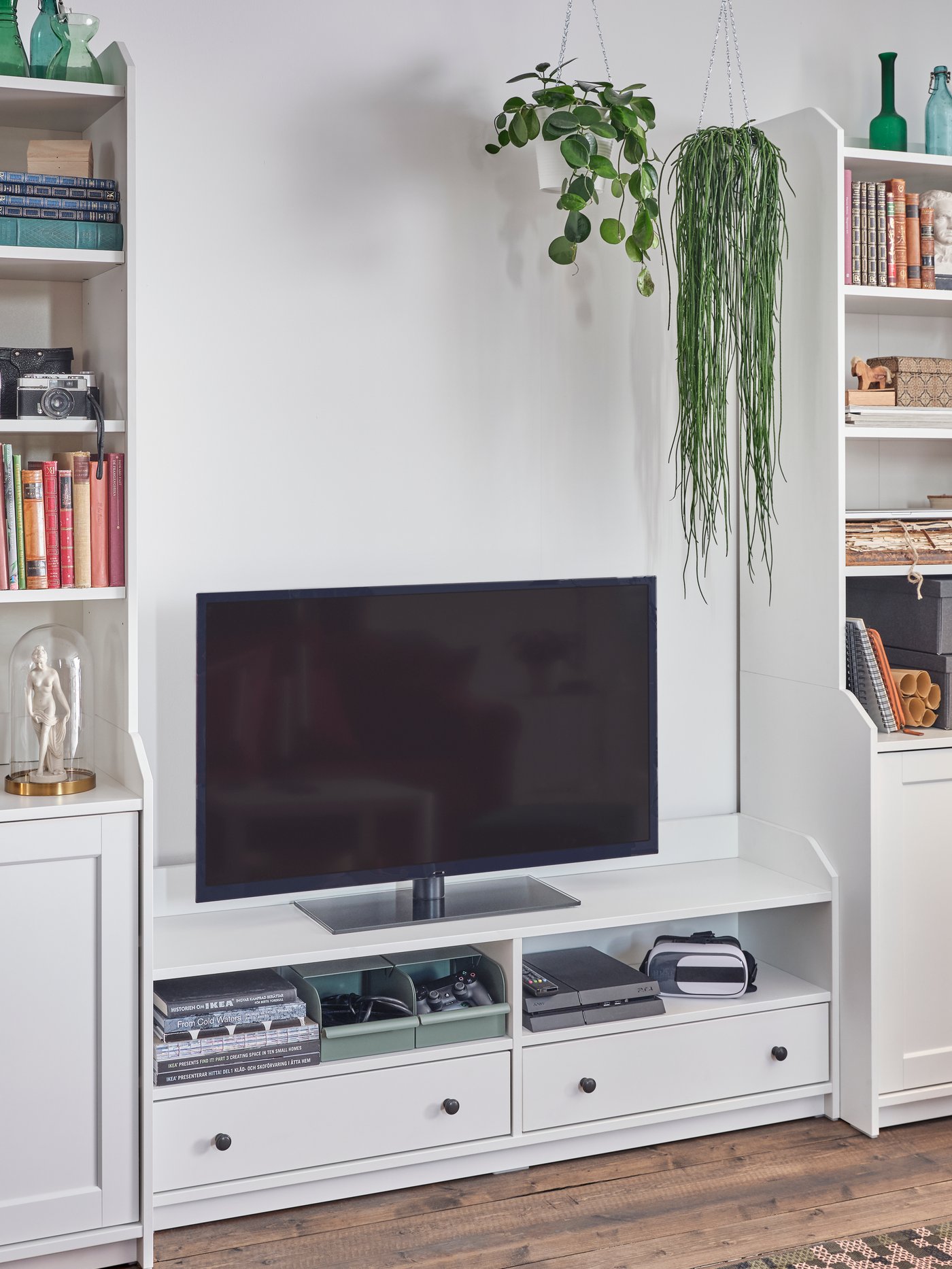 A white HAUGA storage combination with two high cabinets and a TV bench. A TV, a game console and books are here.