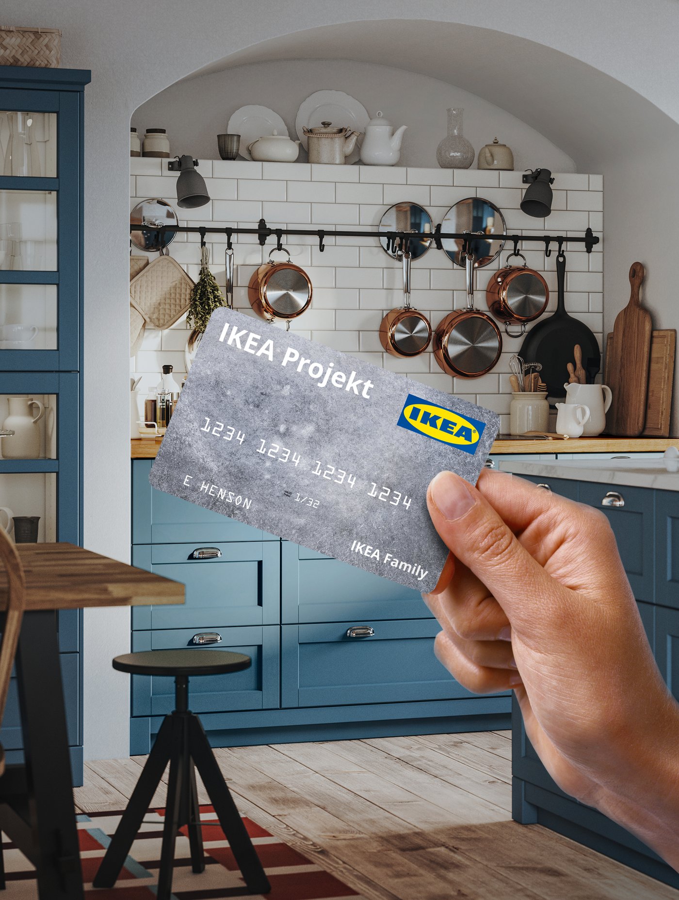 Hand holding an IKEA Projekt credit card in a modern kitchen with blue cabinets and hanging copper cookware.