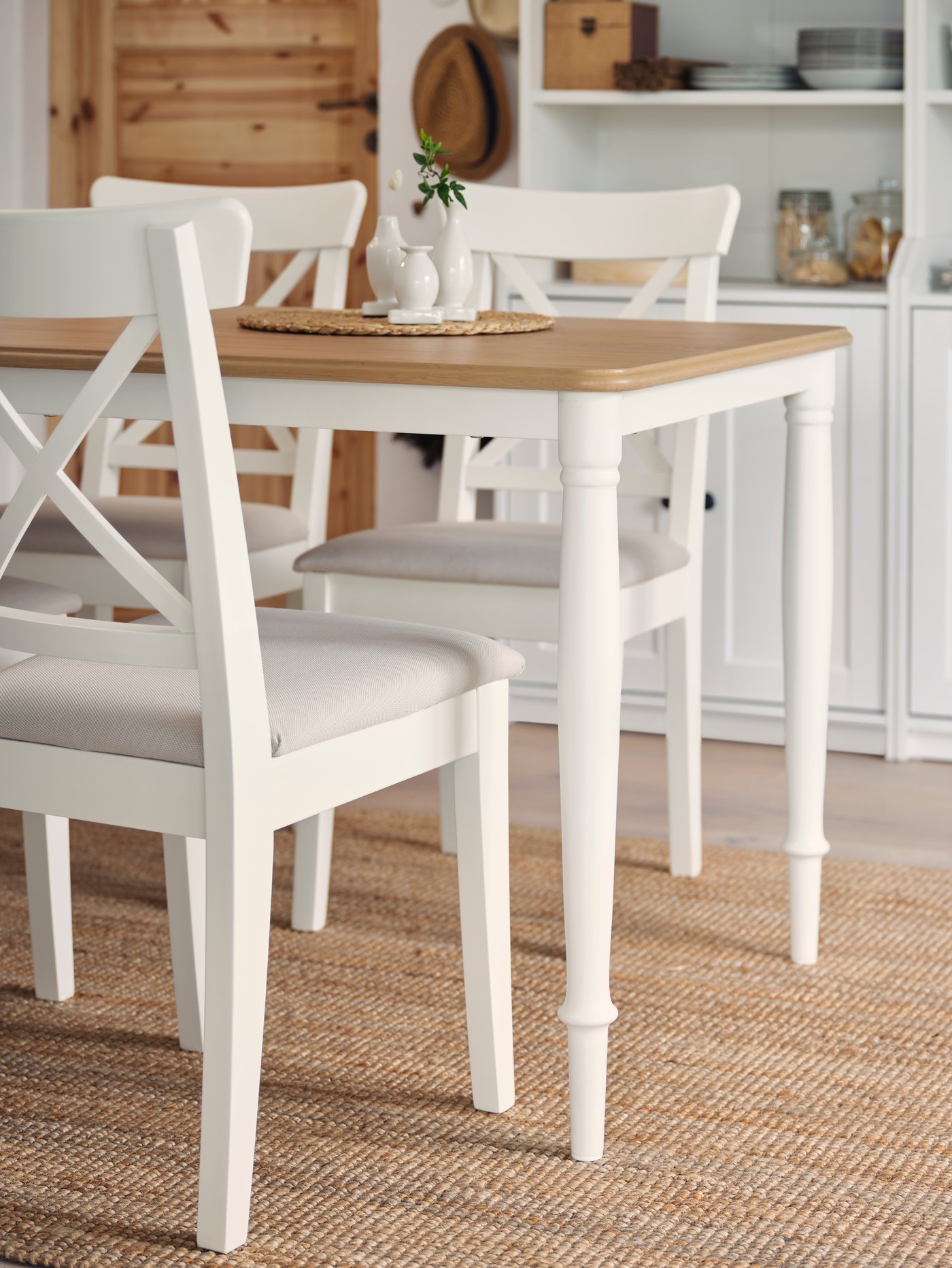 Sillas de comedor INGOLF blancas con cojín gris, frente a una mesa DANDERYD, sobre una tapete de yute.