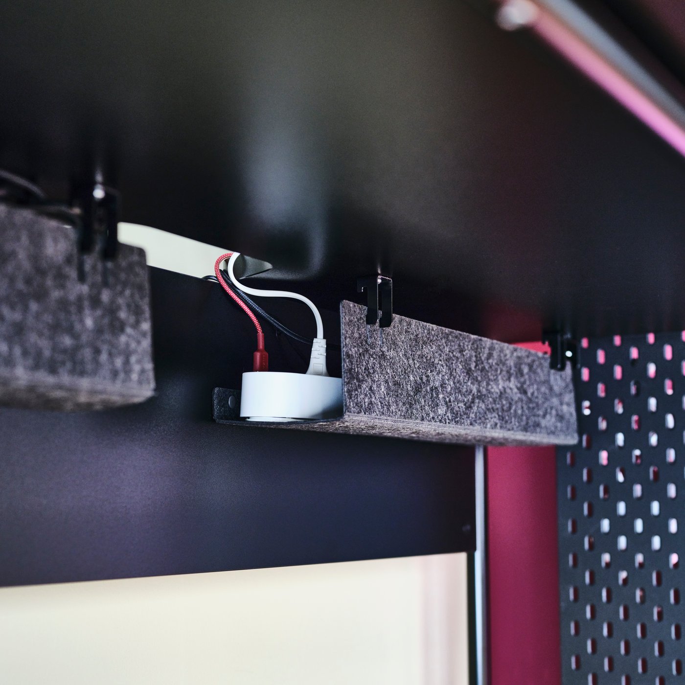 Una regleta KOPPLA de cuatro tomas con dos puertos USB colocada en un compartimento de fieltro bajo la superficie de un escritorio gamer FRÖSKELÅS negro.