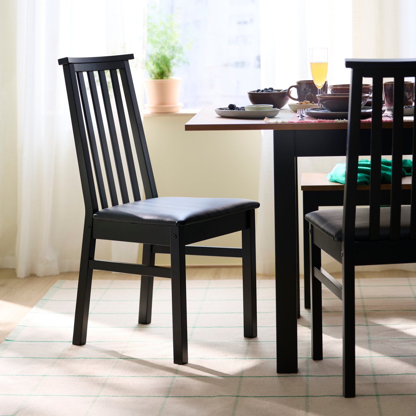 Deux chaises ÅLHULT noires sont disposées à côté d’une table à rallonges ÅLHULT de couleur noire/brun.