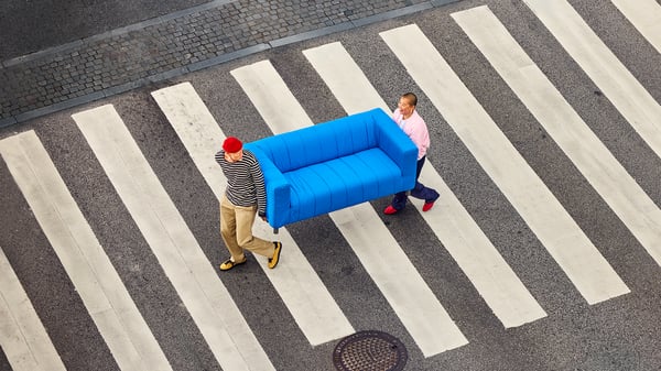 Two people carrying a blue KLIPPAN sofa while crossing the street.