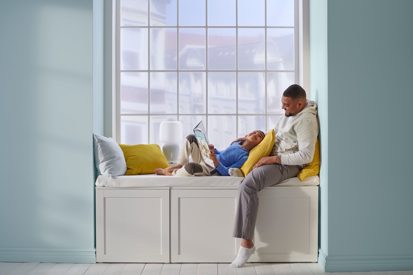 Zwei Personen sitzen auf einer Sitzbank mit vielen Kissen an einem grossen Fenster