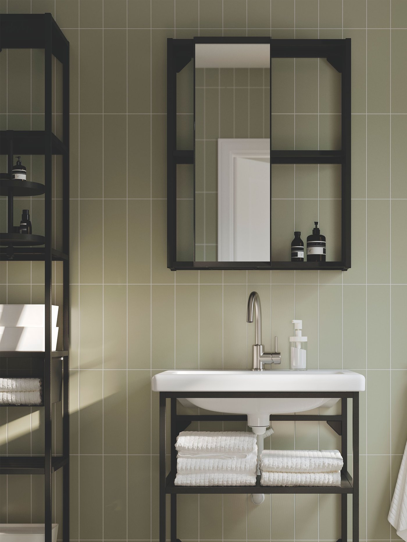 An ENHET bathroom in anthracite with open shelves and a cabinet with a mirror door is placed against a grey-green wall.