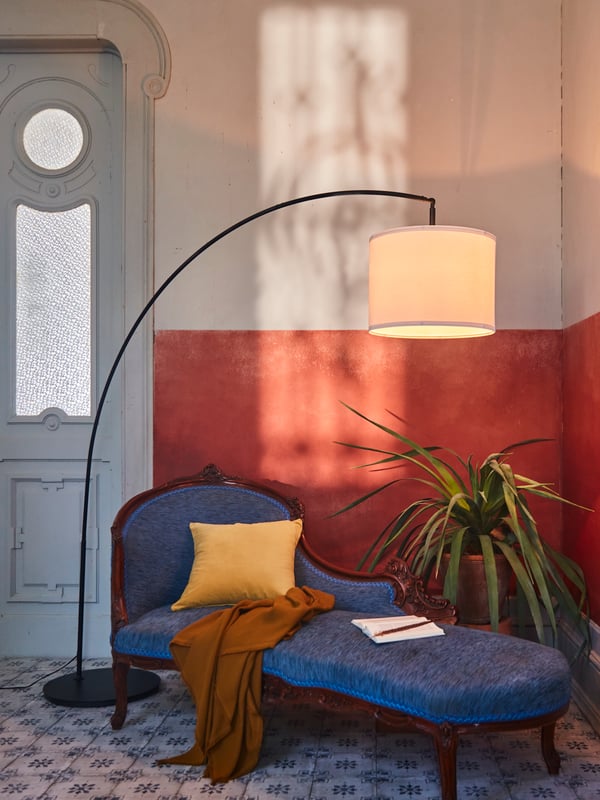 Un pied de lampadaire avec arceau SKAFTET et un abat-jour blanc procurant un éclairage vertical dans un coin au-dessus d’un canapé.
