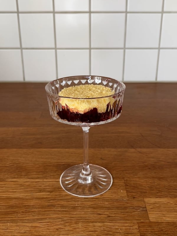 En champagnecoupe med en bit tårtbotten, en klick sylt i och en till bit tårtbotten i.