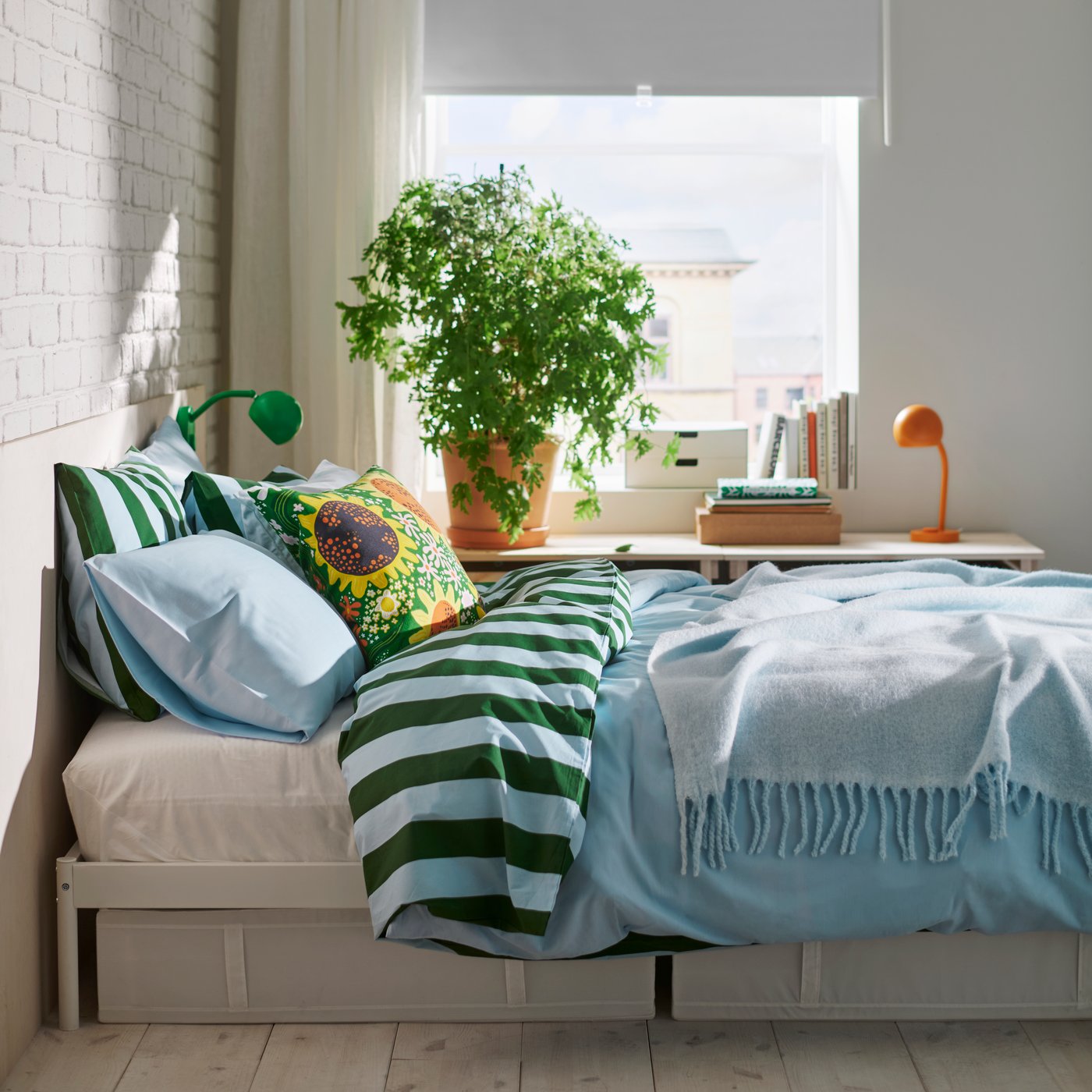 A bright bedroom with a window, plants, and a white bed with blue-and-green-striped SLÅNHÖSTMAL bedding.
