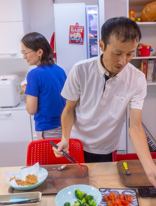 Couple in kitchen, serving up some food at the kitchen table.