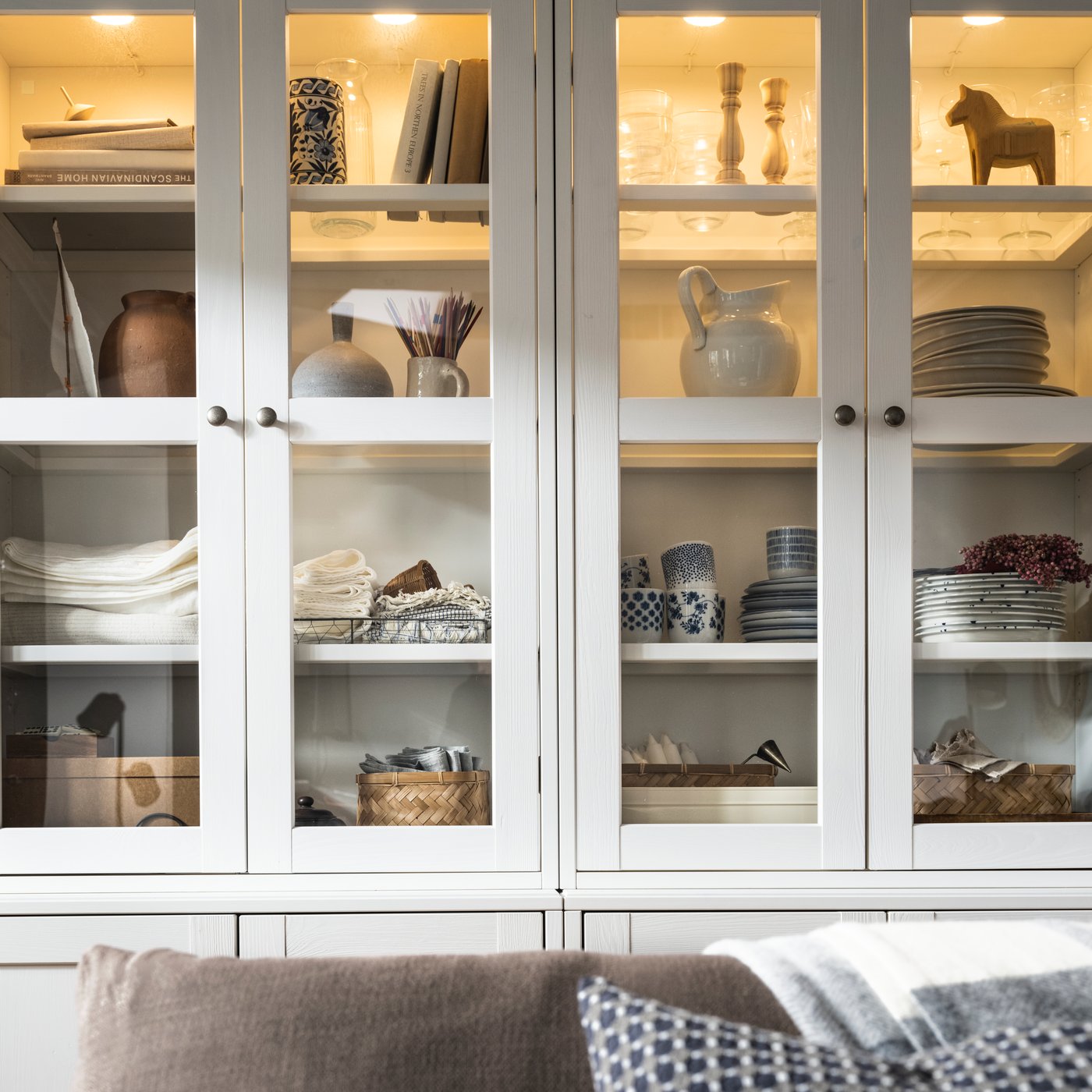 STRIMSÄV LED spotlights are mounted inside HAVSTA storage combinations with glass-doors with many objects on their shelves.
