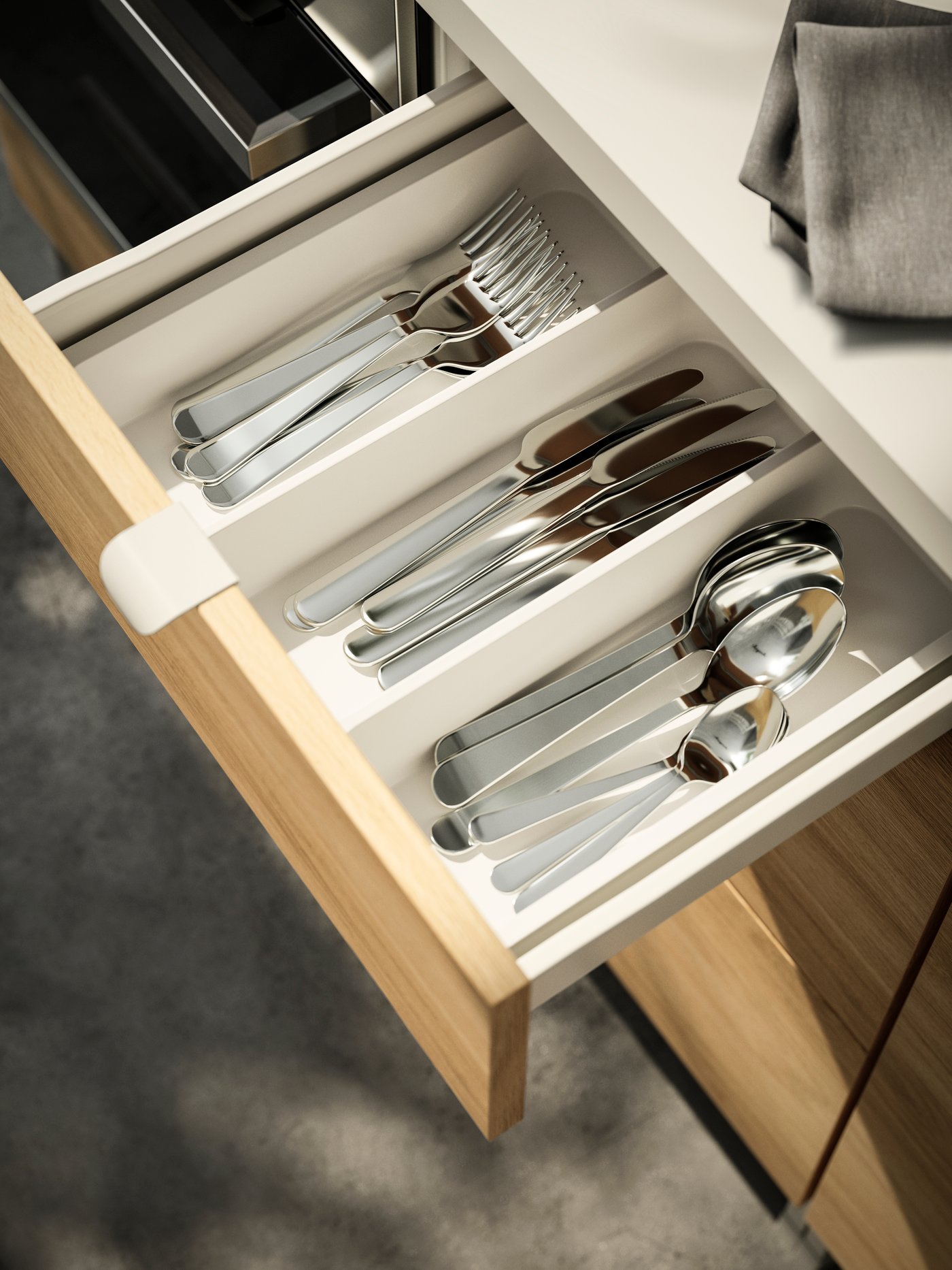 A pulled out ENHET kitchen drawer revealing cutlery in stainless steel, neatly placed in a white STÖDJA cutlery tray.