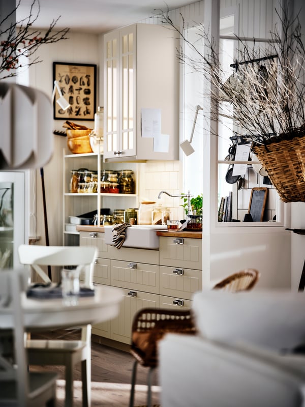A bright, country-style kitchen and dining area, with beige cabinets, a round table and dried branches in a basket.