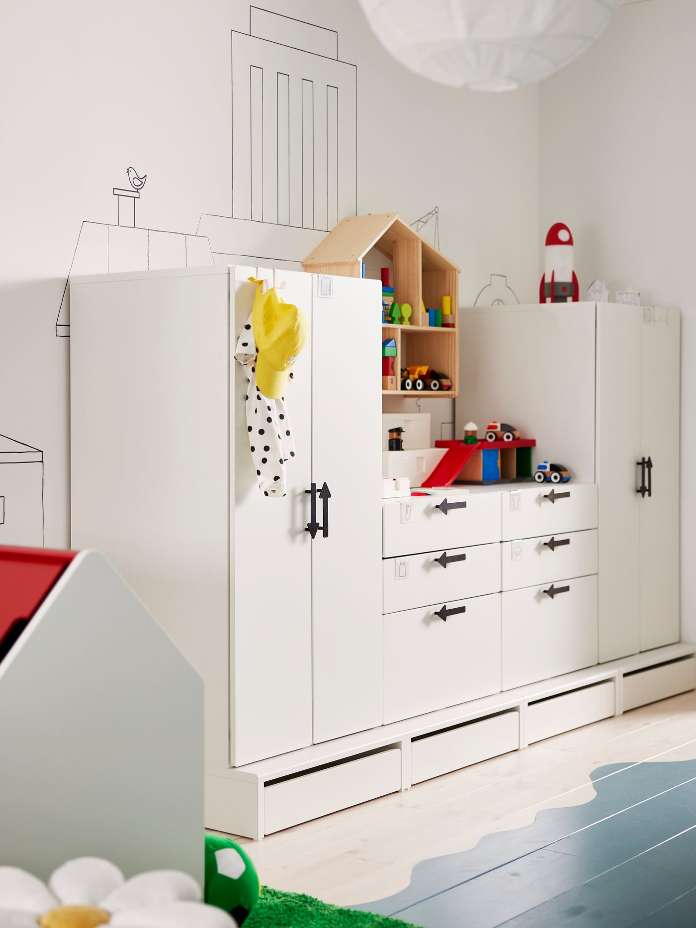 White storage unit in different heights along a wall with painted decorations on it. Blue sea painted on floor.