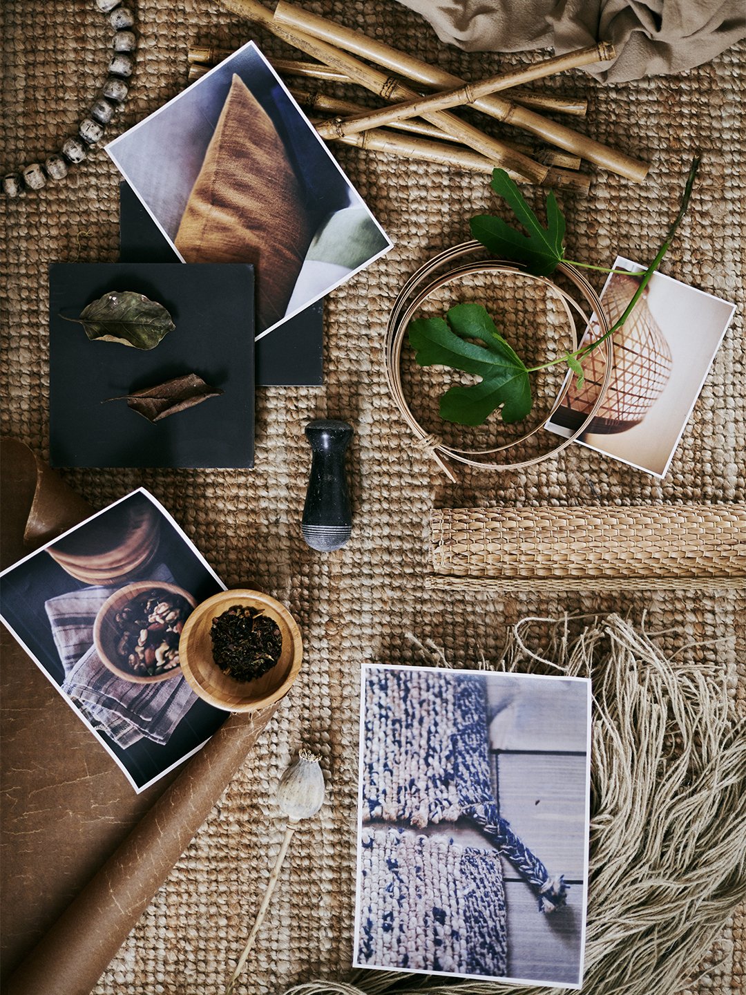 A coarsely woven rug, upon which are several printed pictures plus a variety of raw materials including leaves and wool.