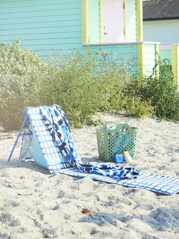 Bain de soleil STRANDÖN bleu et blanc installé sur la plage, recouvert d’une serviette, prêt pour un moment de relaxation au soleil.
