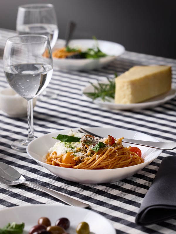 A white OFTAST deep plate is filled with a dish of colourful summer pasta and there’s a SVALKA wine glass with sparkly water.