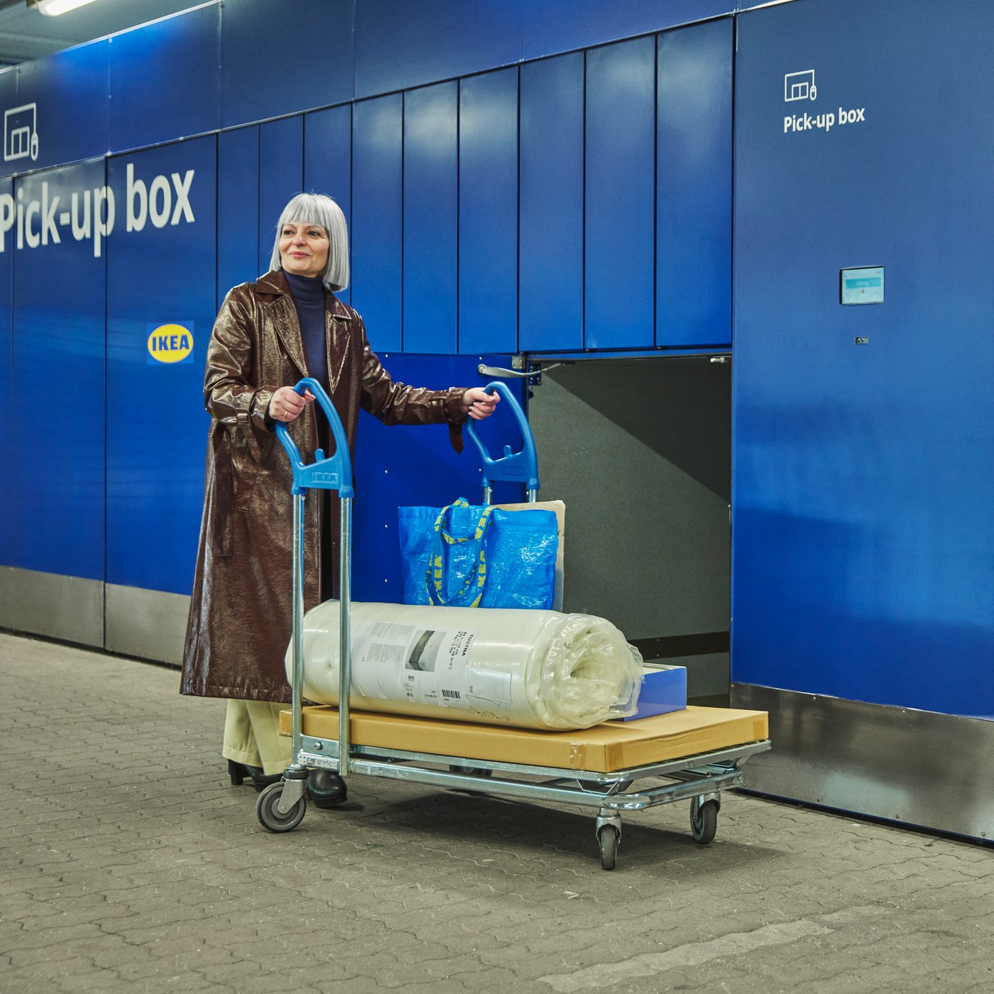 A customer is standing in front of a Click & Collect box, having just collected her order and loaded it onto a trolley