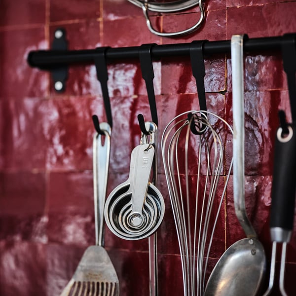 Kitchen utensils hanging from a black HULTARP rail against a red tiled wall.