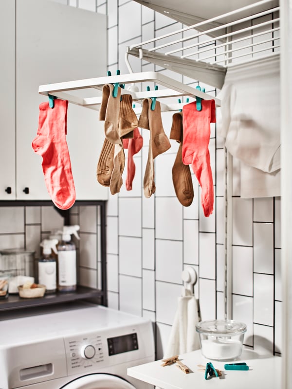 Pink and brown socks hang from a SLIBB hanging dryer with 24 pegs in a laundry room with washing machine and white tiles.