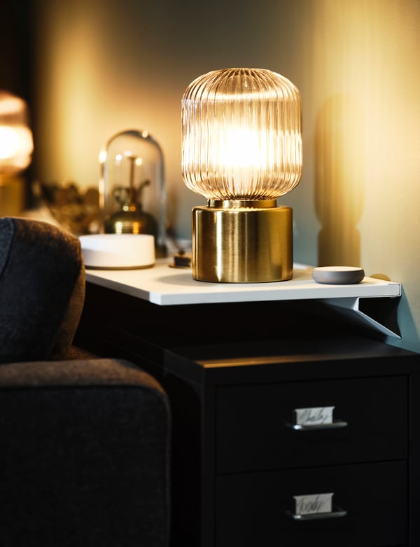 SOLKLINT brass table lamps and other decorative items sit on a wall shelf. Beneath the shelf stands a HELMER drawer unit.