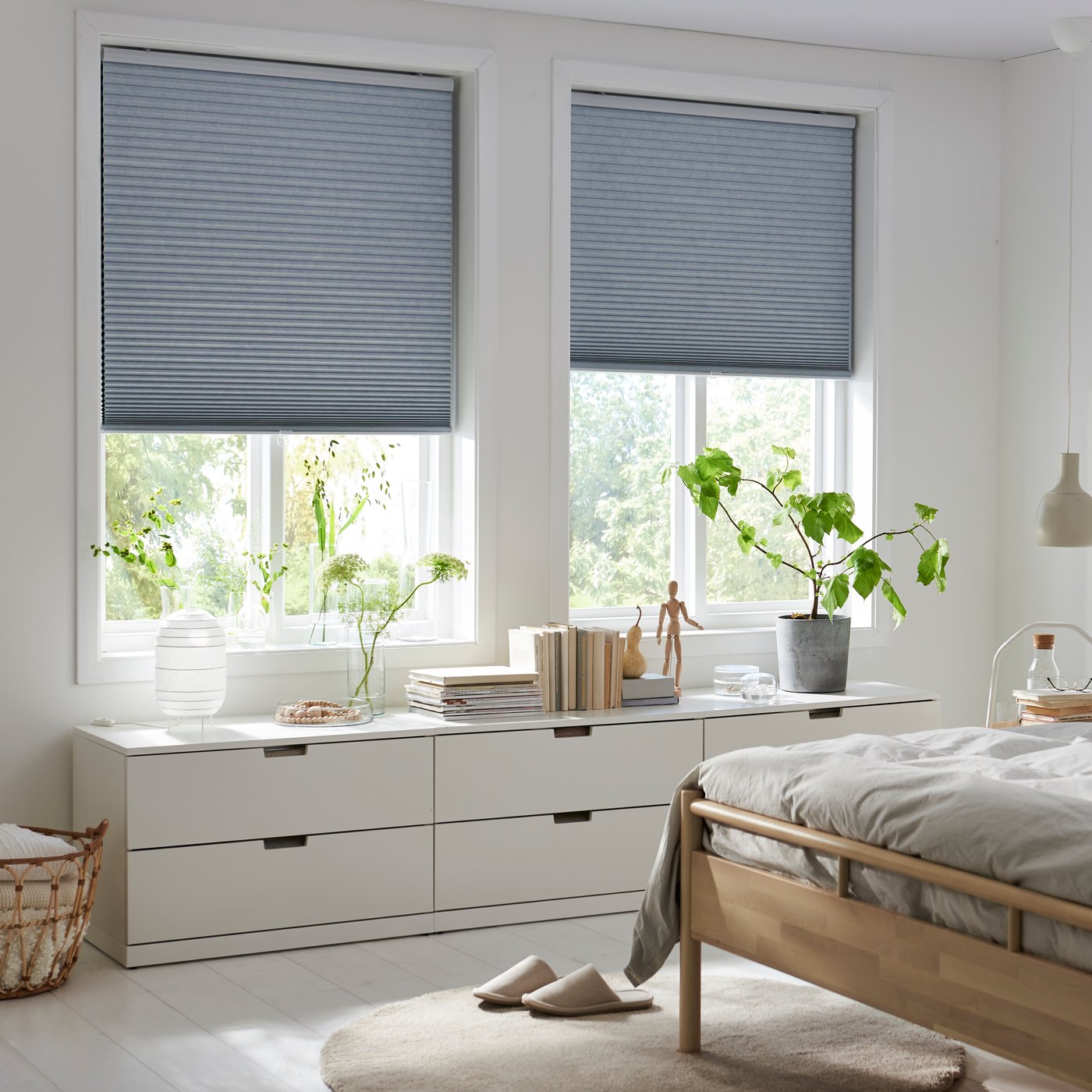 Two windows with TRIPPEVALS cellular blinds half down, BJÖRKNÄS bed frame and NORDLI chest of drawers in a light bedroom.
