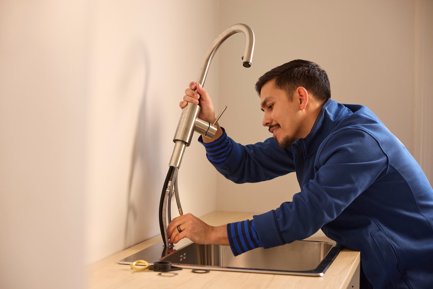 Person installerar en kökskran över en diskho och ansluter slangar underifrån.