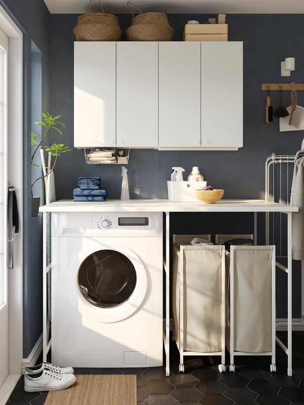 A blue laundry room features a white ENHET storage combination with two laundry bags on castors and a white washing machine.