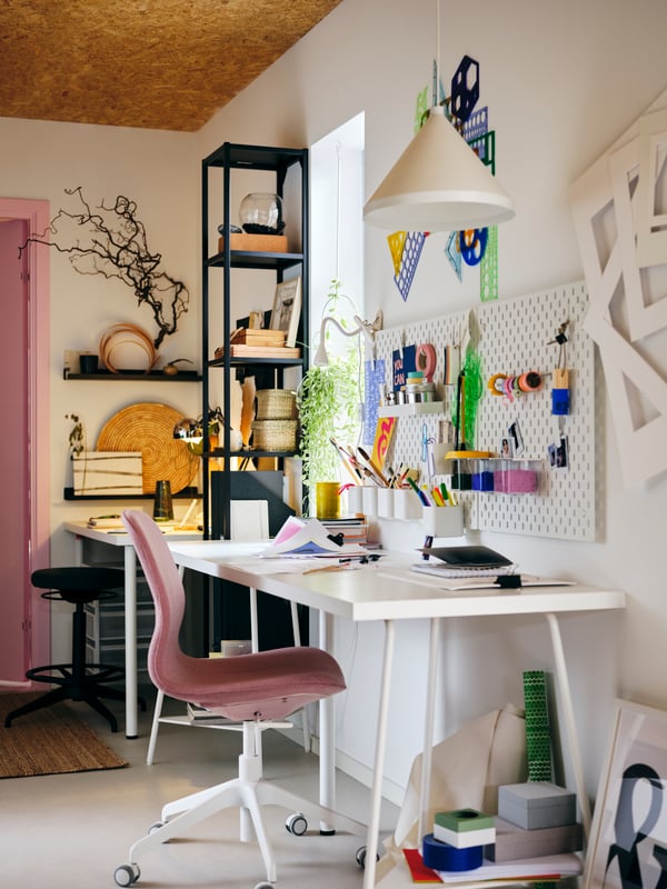 Un espace de travail décoré et coloré s’articulant autour d’un plateau LAGKAPTEN blanc et d’une chaise pivotante LÅNGFJÄLL rose.