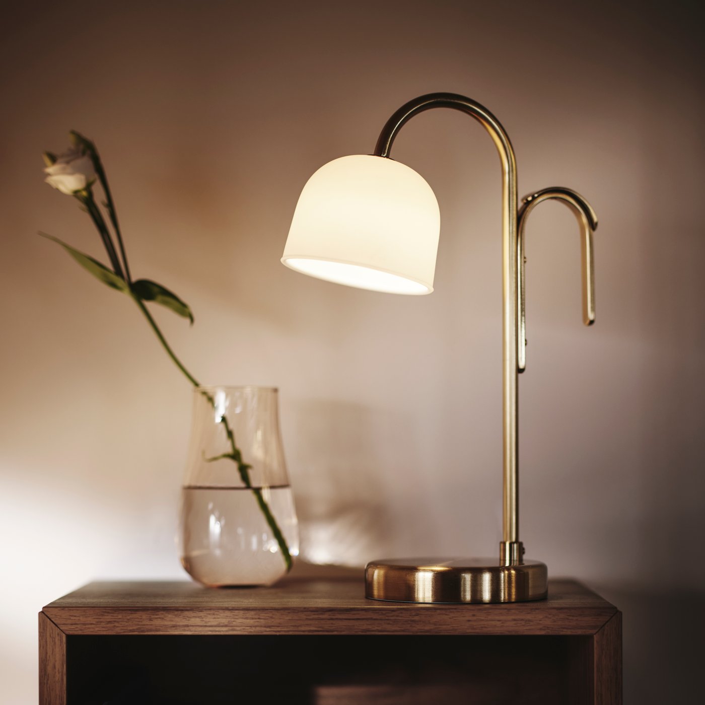 Nærbillede af TVÅMASTAD LED-bærbar lampe foran en glasvase med en blomst. Blødt lys hele vejen rundt.