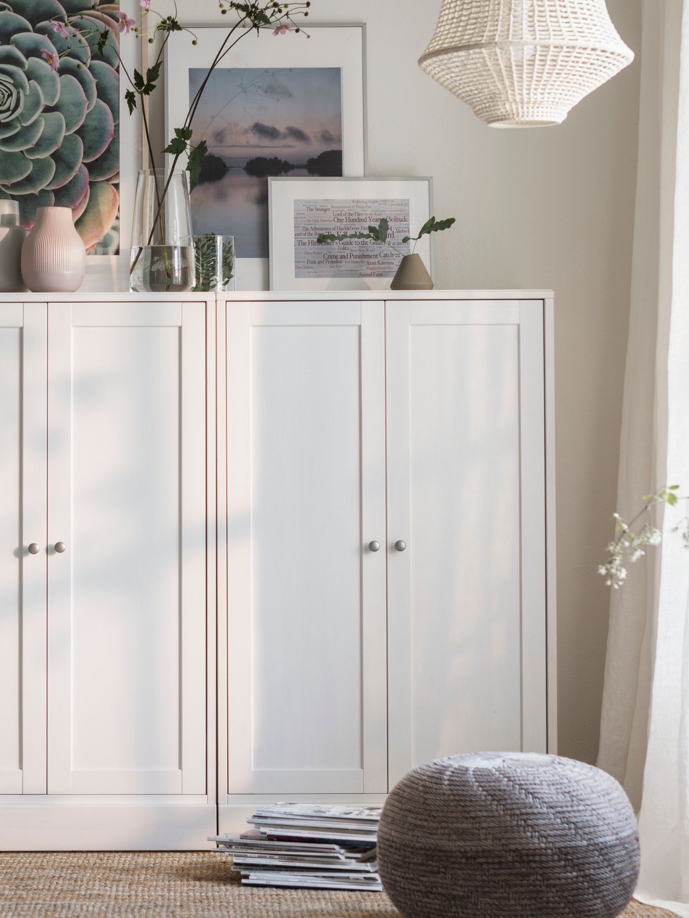 A white HAVSTA cabinet with plinth, with various objects including a lamp and works of art on it, stands against a wall.