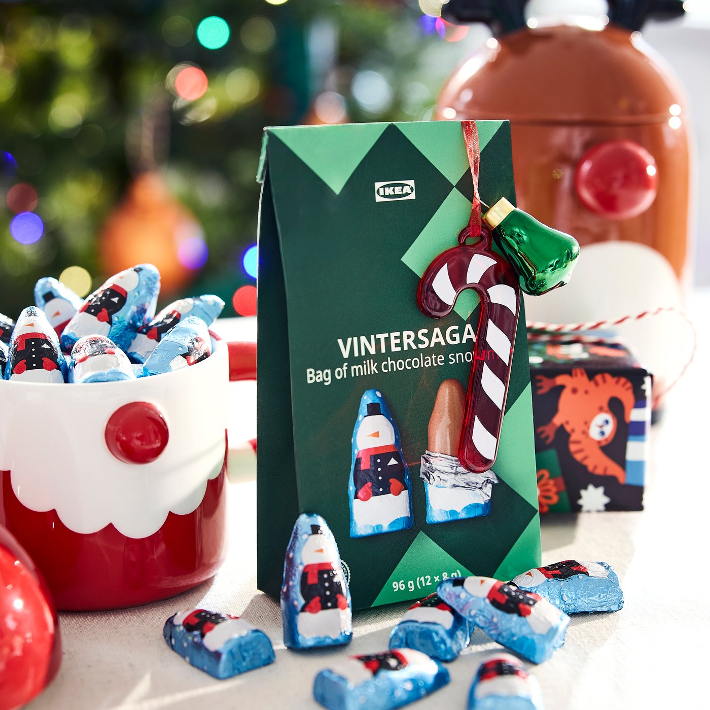 A gift bag of VINTERSAGA milk chocolate snowmen beside a VINTERFINT red santa bowl filled with chocolate snowmen.