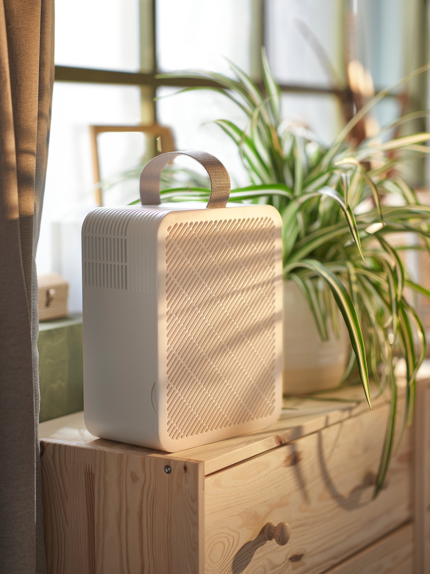 An air purifier placed in a bedroom next to a window and a white nightstand.