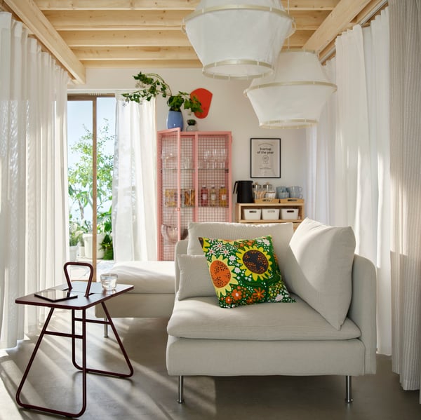A lobby /lounge area with coffee table, white sofas and printed cushion. Behind are a glass cabinet and pine drop-leaf table.