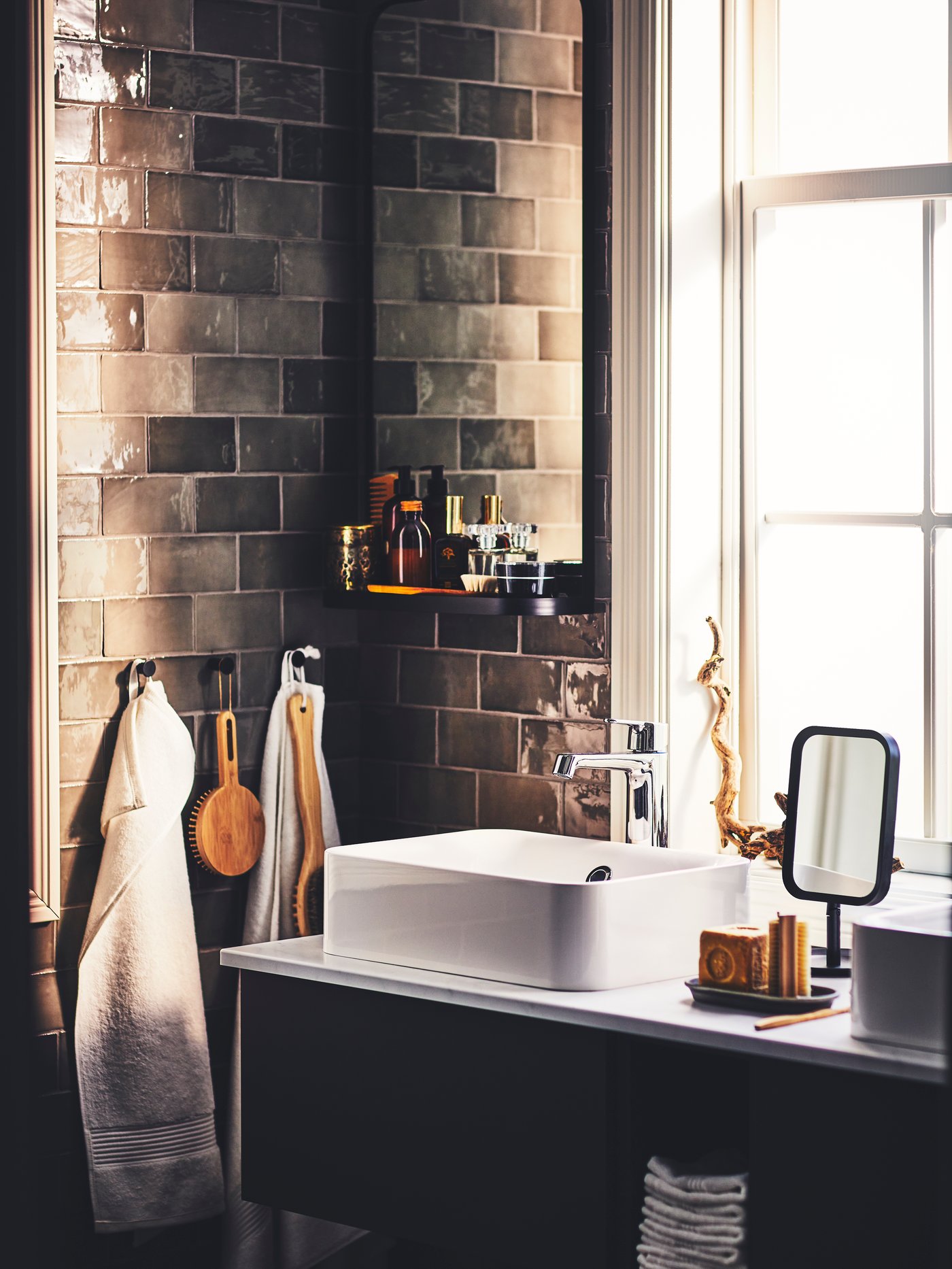 Un cuarto de baño con un lavabo GODMORGON gris oscuro, un espejo de mesa LINDBYN negro y objetos colgados de ganchos SKOGSVIKEN.