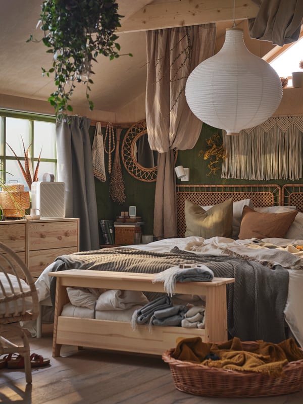 Spavaća soba s boho atmosferom i dve RAST komode s 3 fioke pored kreveta s uzglavljem od ratana i RISBYN abažura visilice.