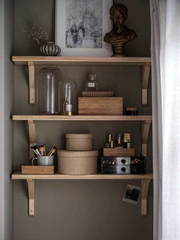 A recess fitted with wall-mounted TRANHULT/SANDSHULT shelves with framed art, glass domes and other decorative items.