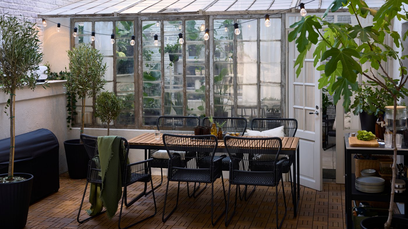 VÄSMAN uitschuifbare tafel en zes TALLSKÄR stoelen met armleuningen staan op RUNNEN vlonders in acacia op een terras.
