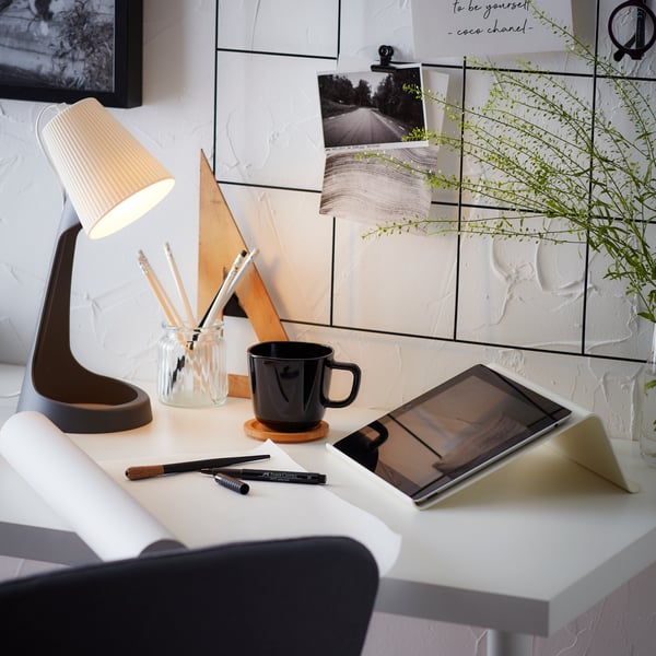 Photos et citations sur un tableau mémo noir SÖSDALA avec des pinces au-dessus d'un bureau équipé d'une lampe de bureau SVALLET, d'une tasse et d'un support pour tablette.