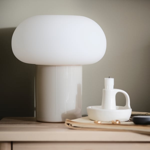 An opal-and-white DEJSA table lamp stands next to a white candlestick.
