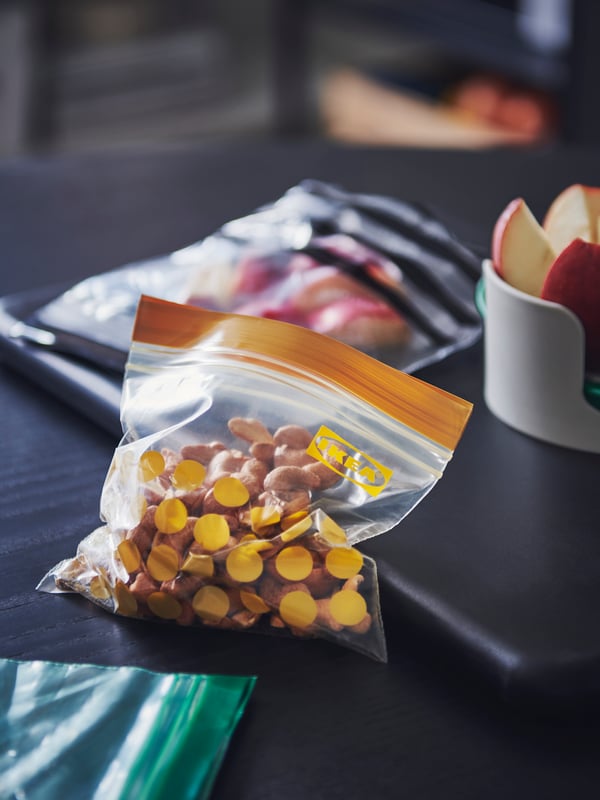 Three ISTAD resealable bags in various sizes holding diverse food items on a dark wooden surface, a folder and other items.