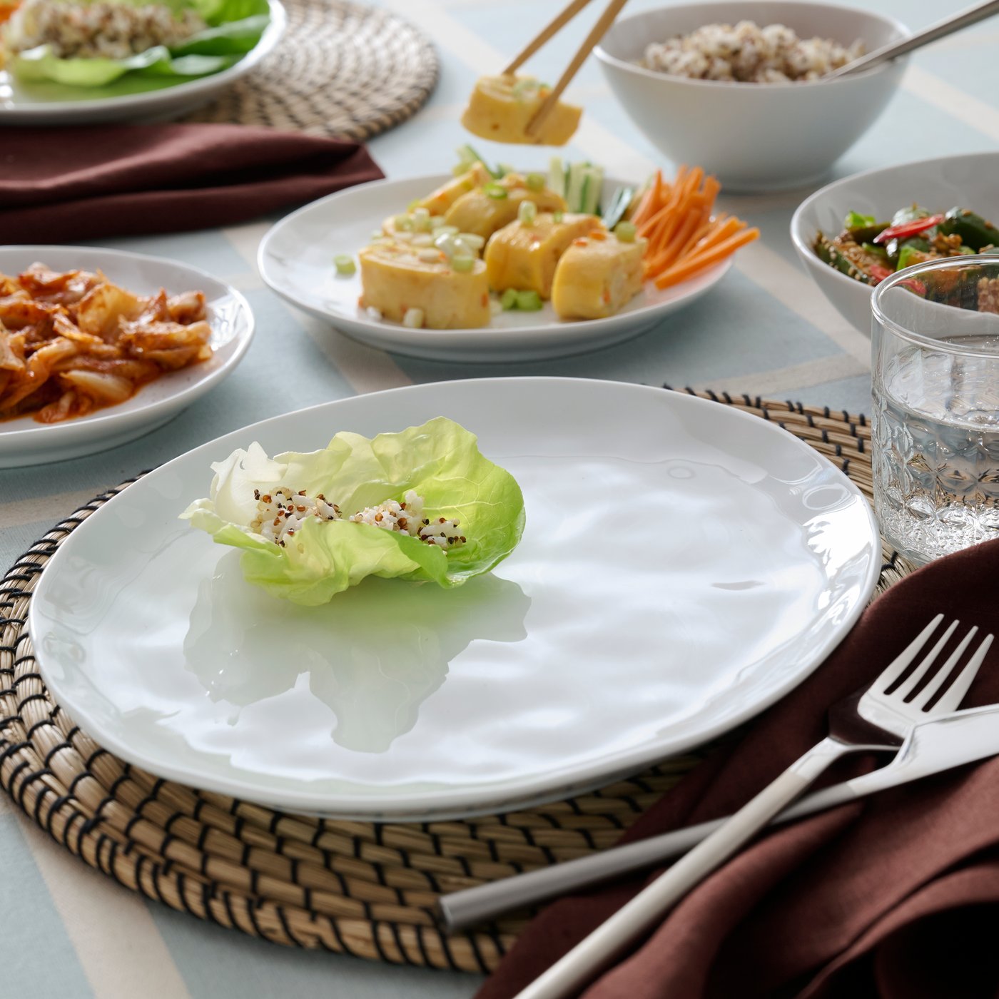 A white FORELLTETRA plate has a leaf of lettuce on it and there are also side plates and bowls with food on the table.