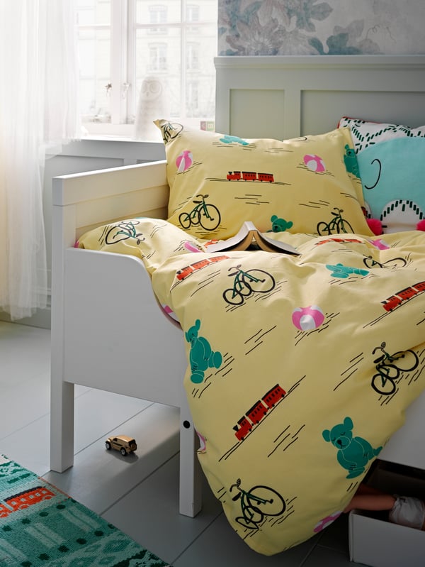 Part of a SUNDVIK extendable bed with colourful KÄPPHÄST bed linen and a KÄPPHÄST cushion lying on top of it.