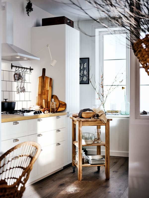 A country-style kitchen with a light wood counter top and white cabinets, and a birch trolley holding dishes and bowls.